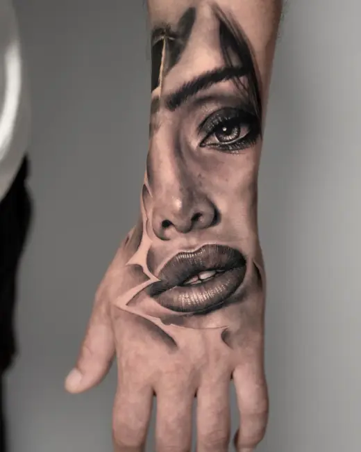 Black-and-grey realism tattoo of a woman’s face across the forearm and hand