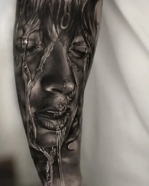 Black-and-grey realism tattoo of a crying face with reflective liquid details