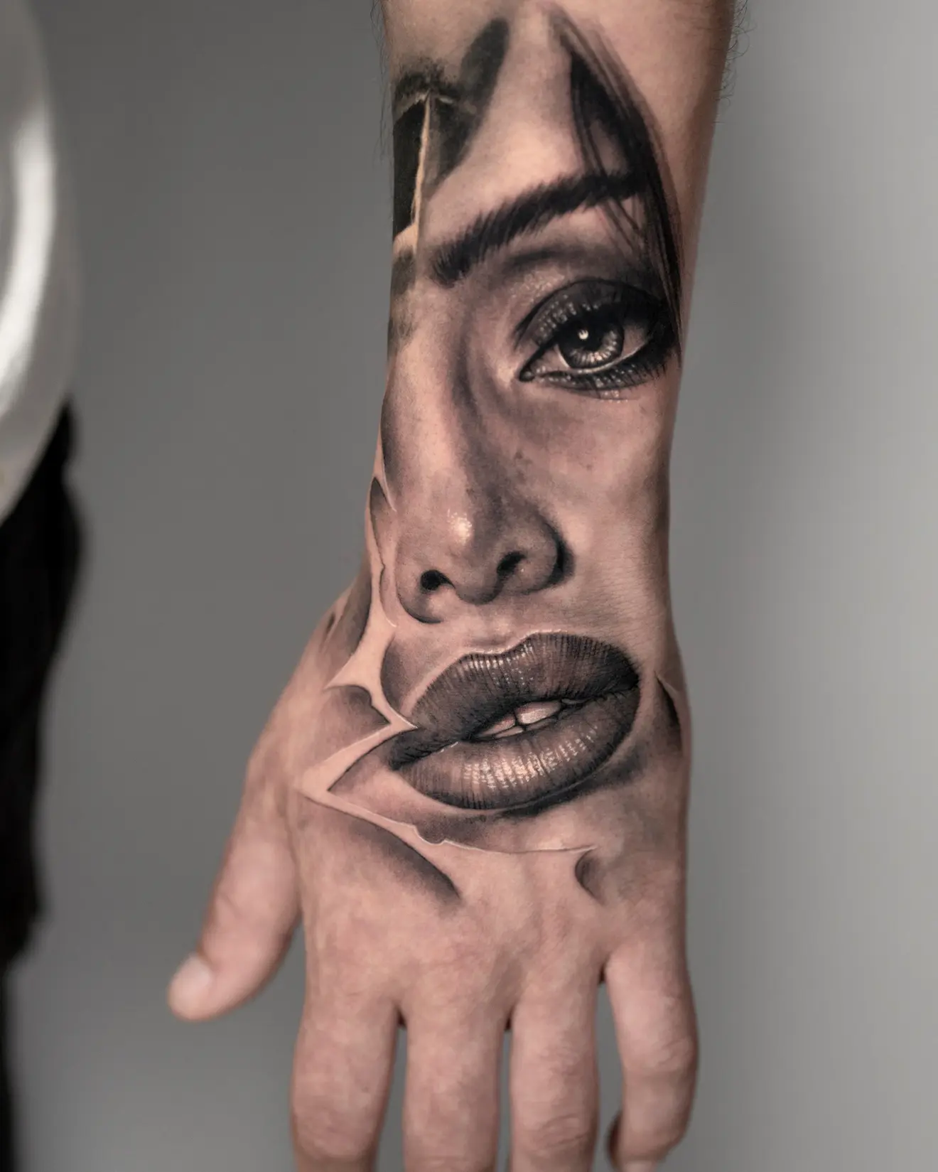 Tatuaje realista en black and grey de un rostro femenino sobre el antebrazo y la mano