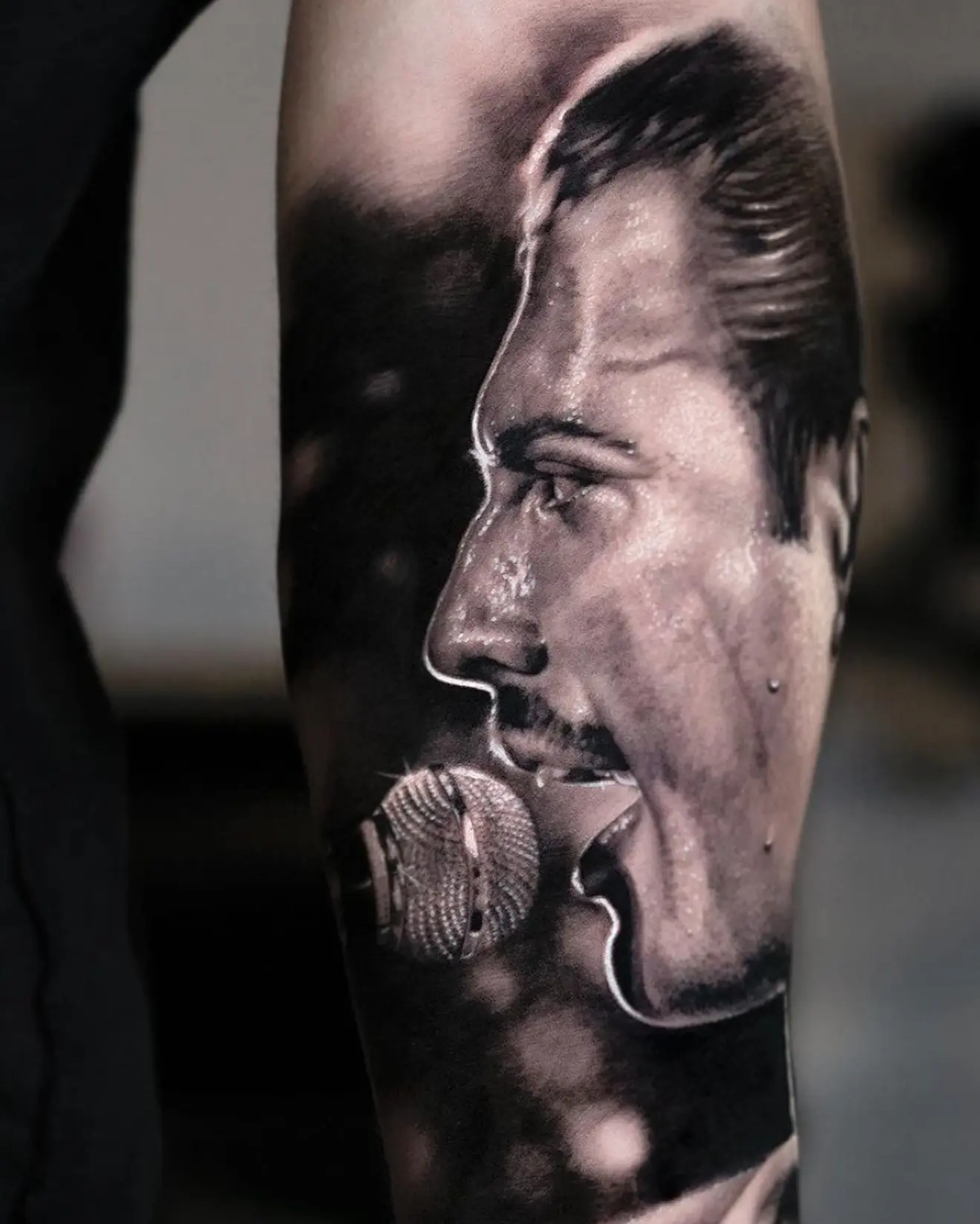 Tatuaje realista en black and grey de Freddie Mercury de perfil ante un micrófono