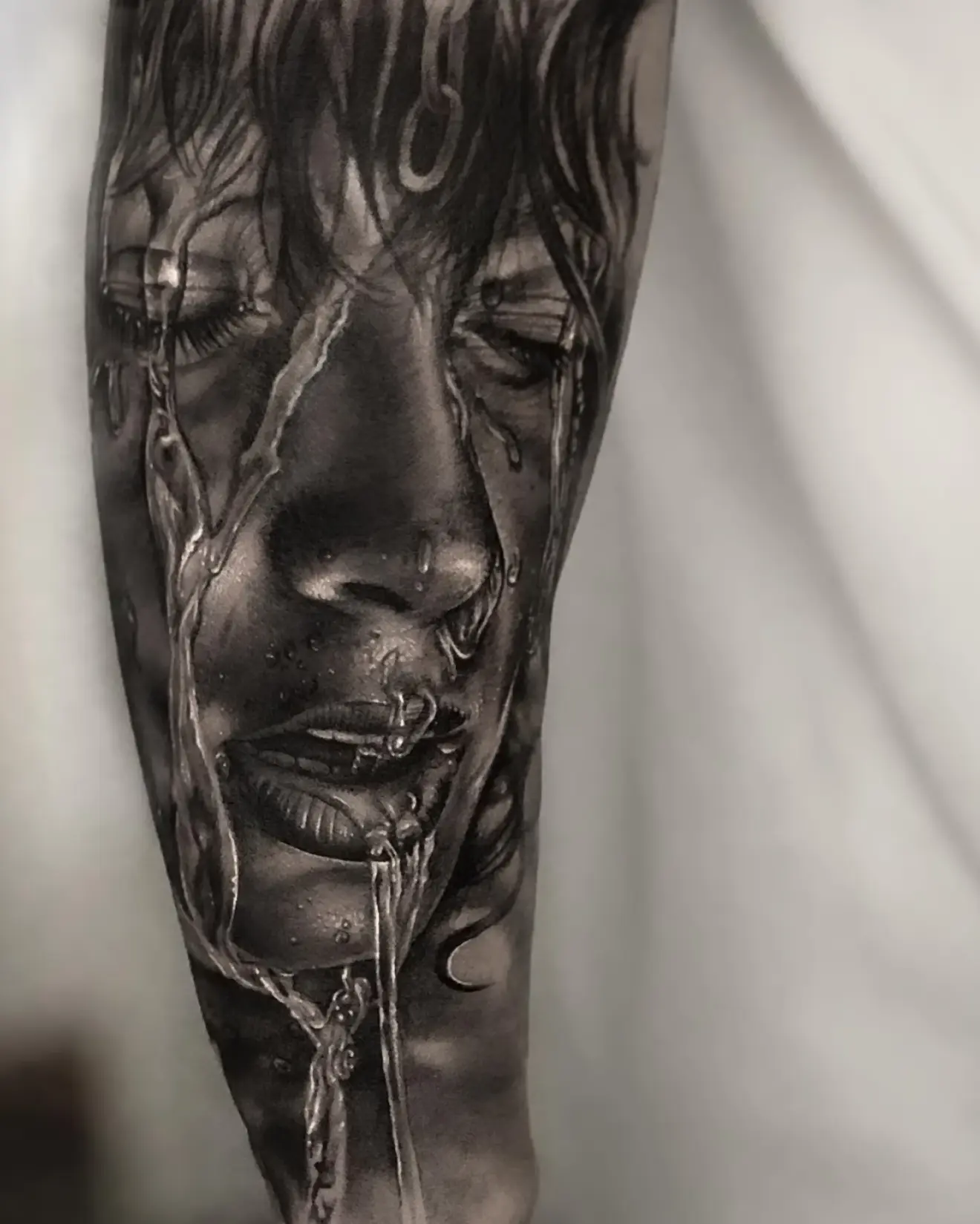 Tatuaje realista en black and grey de un rostro llorando con reflejos líquidos