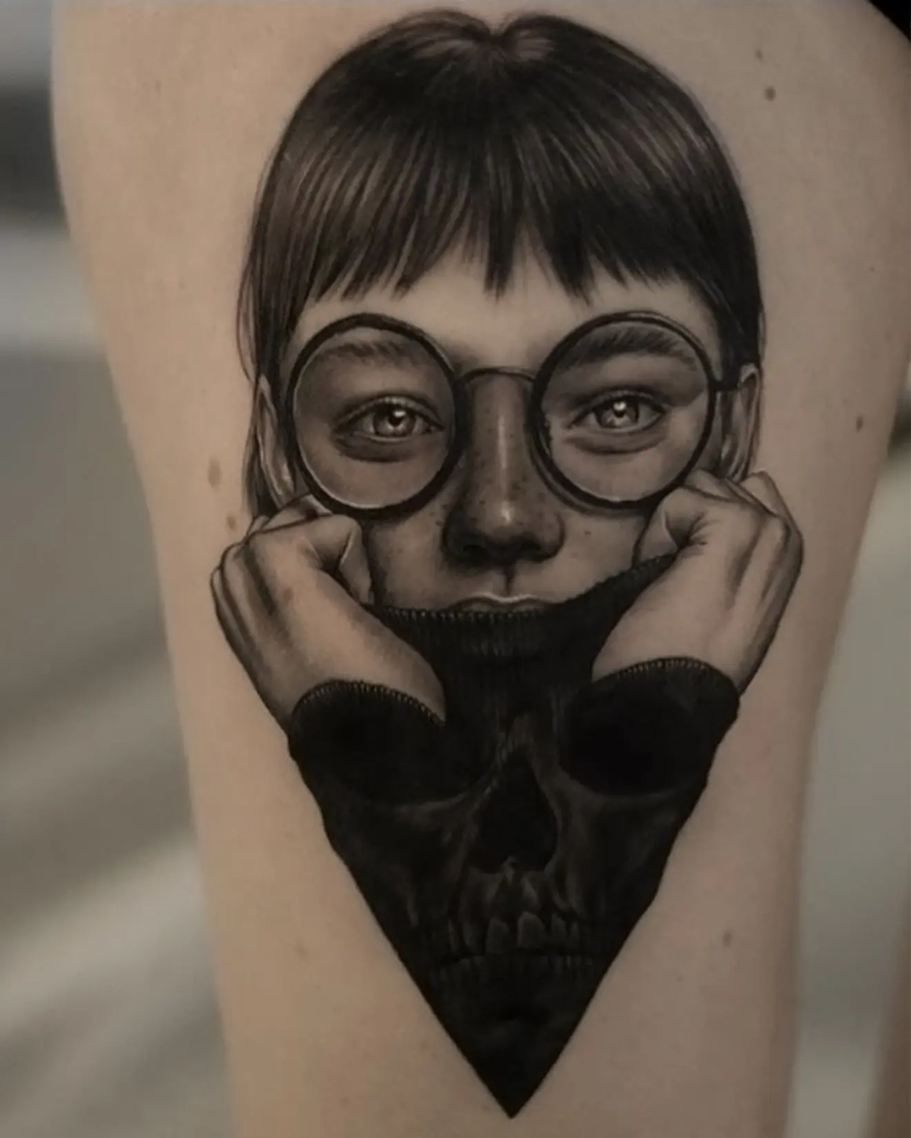 Tatuaje realista en black and grey de una mujer con gafas y un jersey que forma una calavera